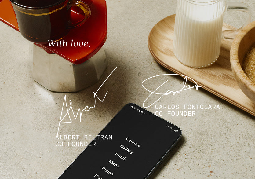 Smartphone on a table with coffee and milk, featuring co-founder names and signatures.