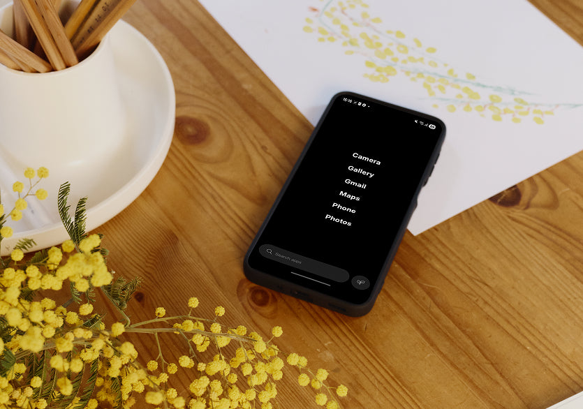 Smartphone on a wooden surface with yellow flowers and a vase in the background