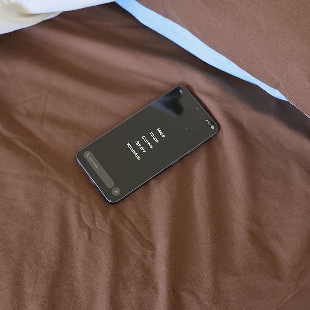 A Balance Phone lying face up on a brown bedsheet, its screen showing a short app list: Maps, Phone, Camera, Spotify and WhatsApp.