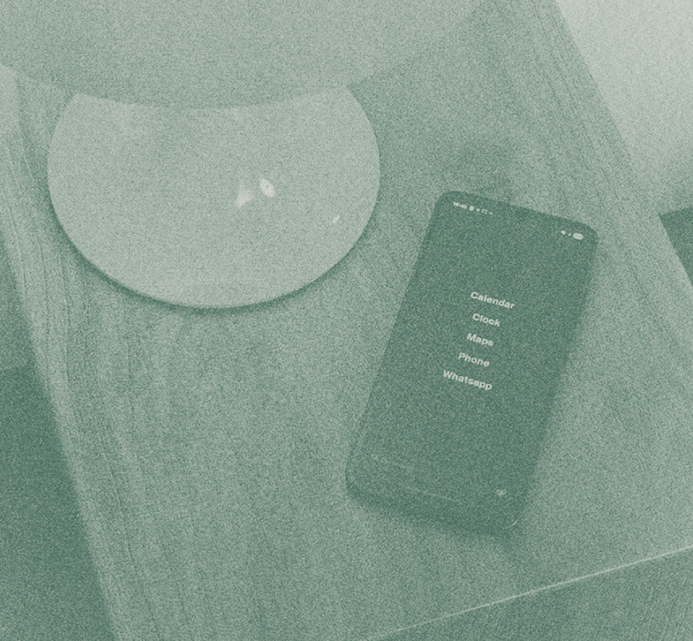 A smartphone placed next to a rounded leather pouch on a wooden surface, showing a simple screen with a list of items