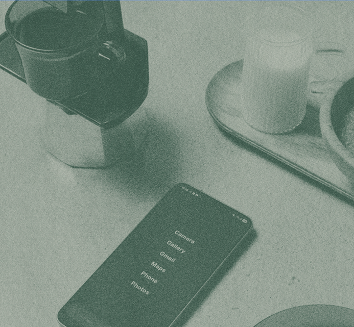 A smartphone lying on a table alongside a camera, a coffee mug, and a glass of milk, capturing an everyday café moment