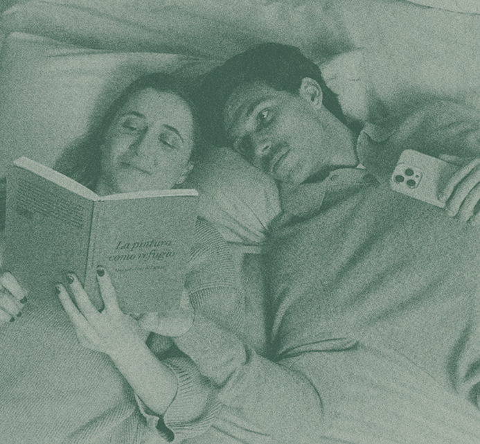 A couple lying in bed together, the woman reading a book while the man rests beside her, sharing a quiet and intimate moment