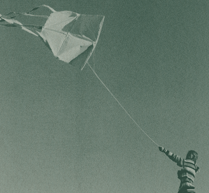 A handmade kite flying against a clear sky, held by a string from below