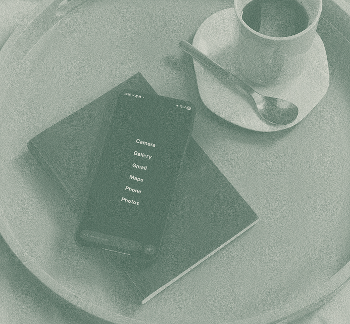 A smartphone and a notebook resting on a round table next to a cup of coffee and saucer, in a calm café setting