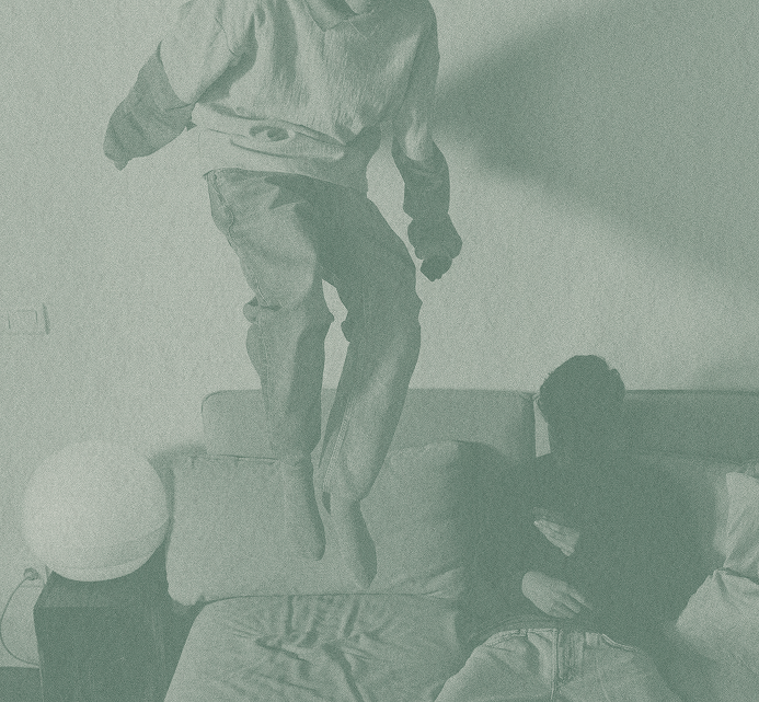 A child jumping energetically on a bed while another child watches, capturing a playful and carefree moment at home