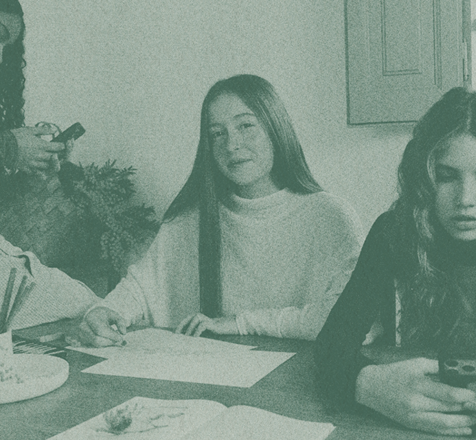 Three young women sitting together at a dinner table with plates of food, engaged in conversation during a meal