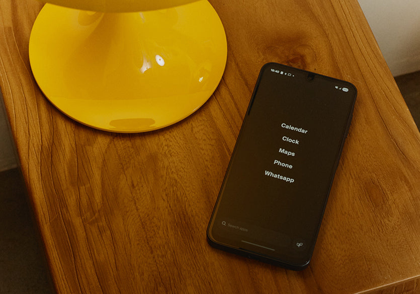Smartphone with app icons on a wooden surface next to a yellow electronic device.
