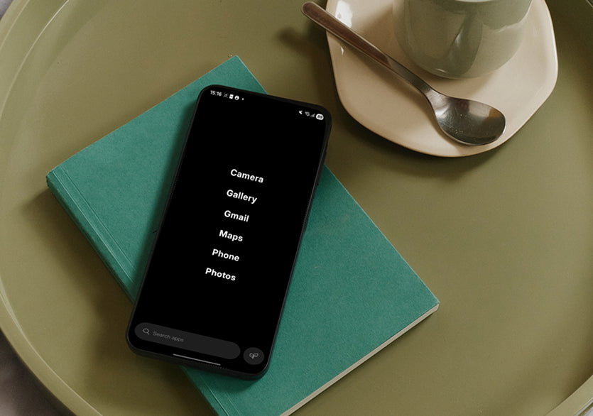 Phone with app list on a teal book next to a cup and saucer on a green surface