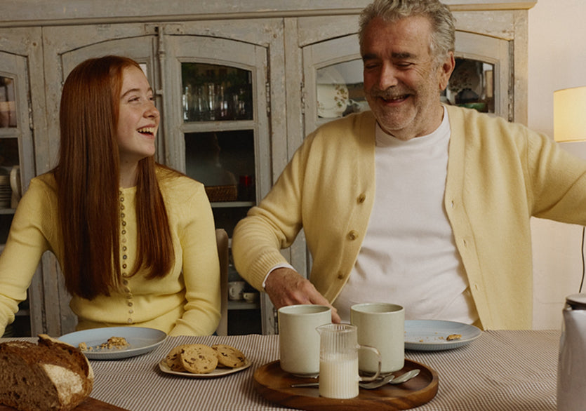 Man and woman sitting at a table with coffee and snacks, smiling and laughing.