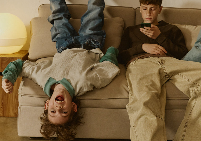 Two children on a couch, one upside down and the other using a phone.