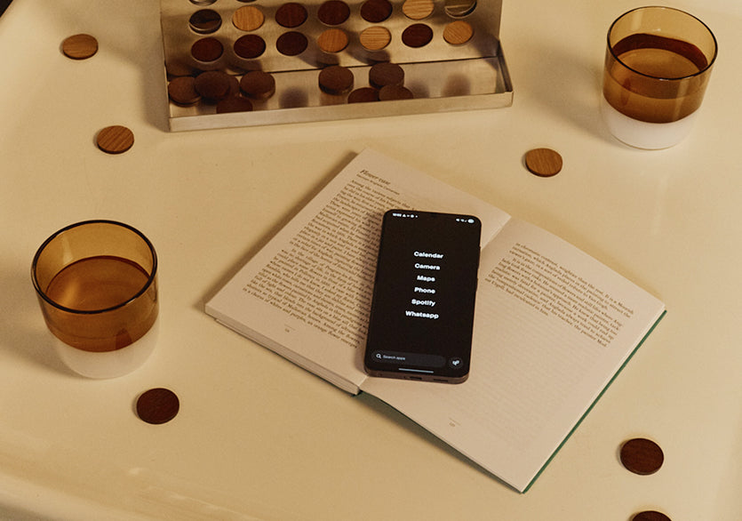 Phone on an open book with coins and glasses around on a light surface