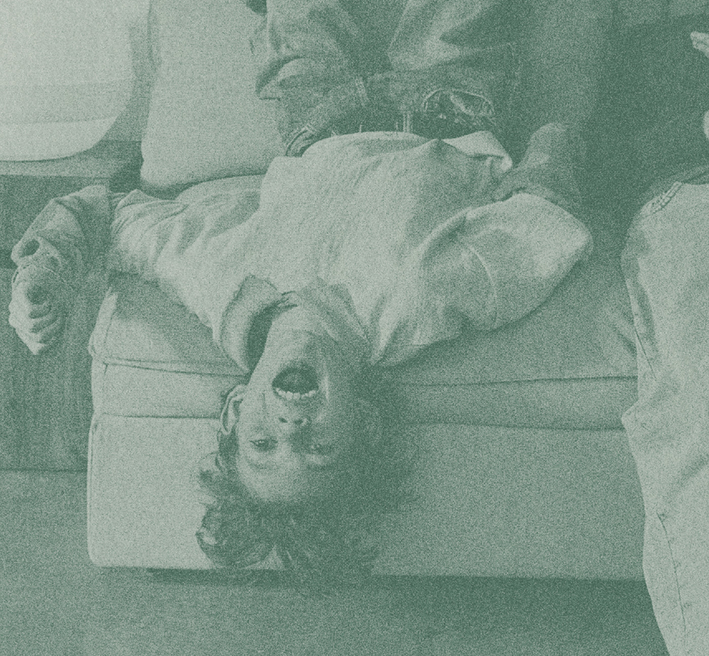 Person lying on a couch with another person standing over them, in a grayscale filter.