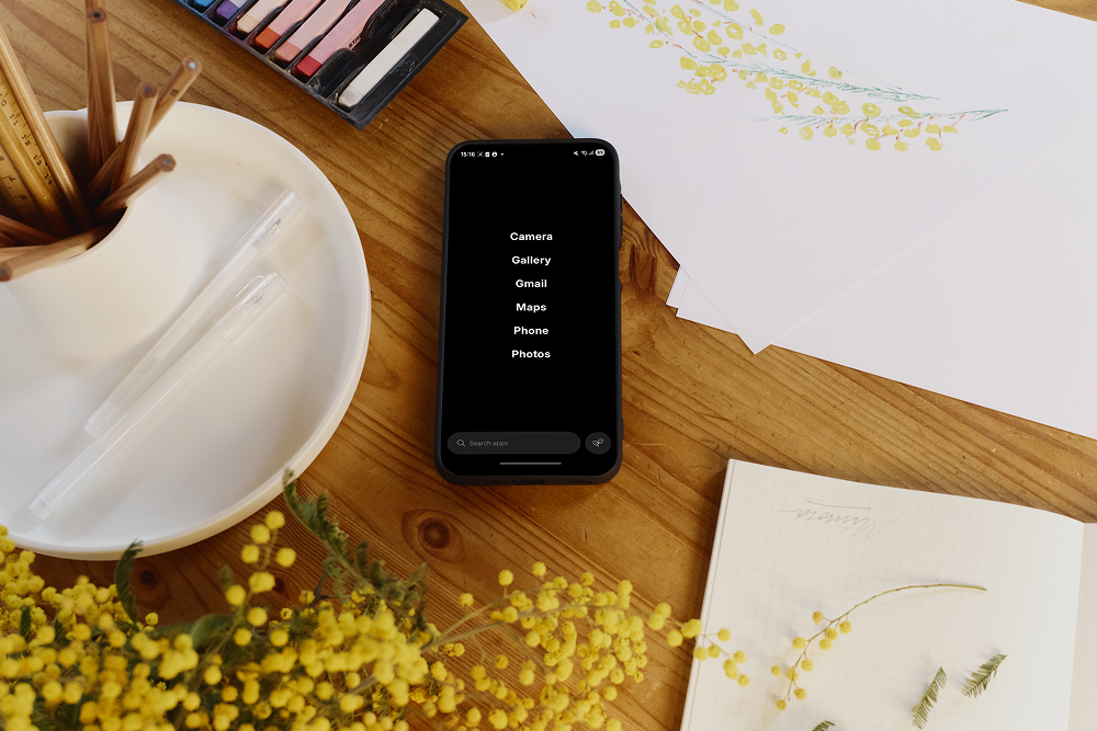 Smartphone on a wooden table with floral decorations and stationery items.