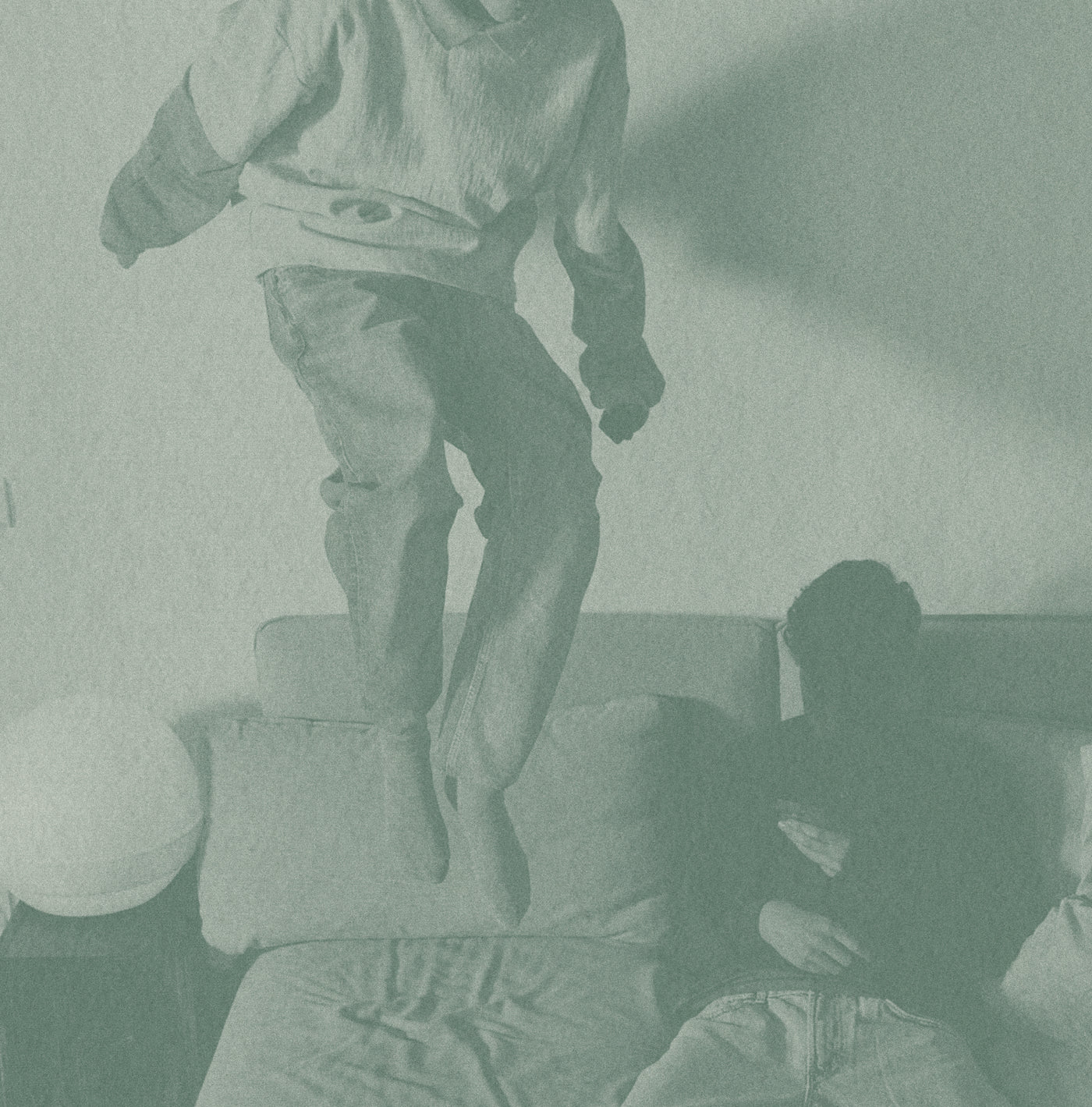 Person standing on a couch with another person sitting on a chair in a dimly lit room.