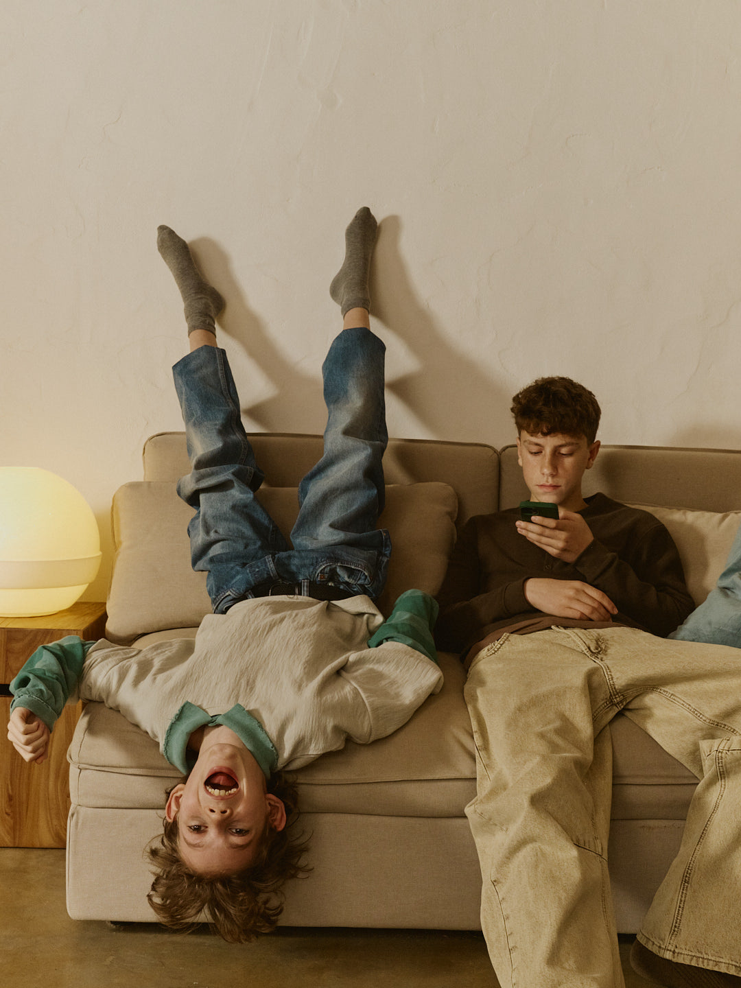 Child upside down on a couch with another person sitting next to them, using a phone.